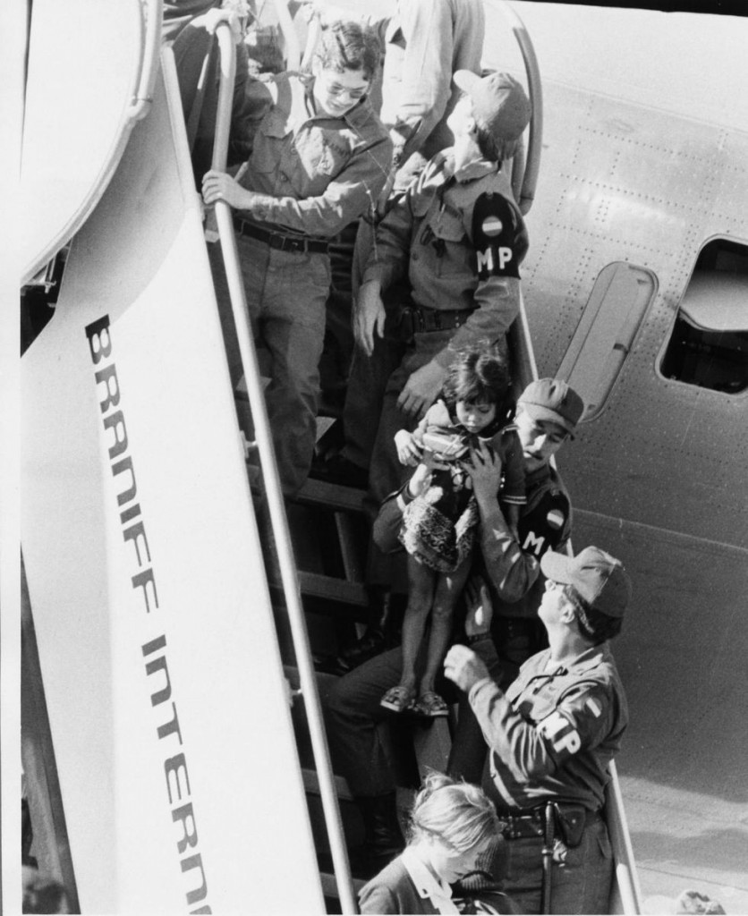 Nhân viên quân sự Mỹ bồng em bé Anne-Pham, 3 tuôi, xuống cầu thang máy bay tại Fort Chaffee, Arkansas vào tahsng 5, 1975. Anne D. Phạm là tác giả bài Finding My Heroes, Finding Myself: From Refugee Child to State Department Official Nguồn: Quân đội Hoa Kỳ.